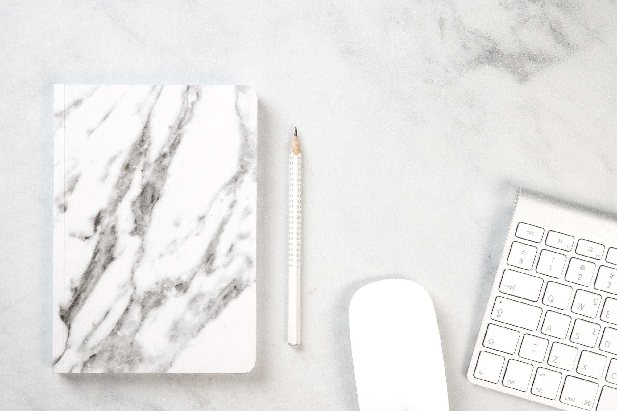 White stationery on a white marble desk. Marble notebook, keyboard, mouse and a pencil